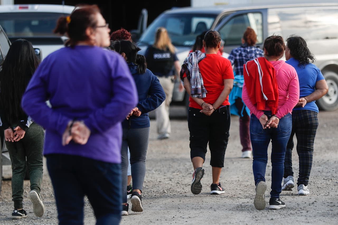 Una fila de mujeres con sus manos atadas es conducida a los autobuses de ICE donde serán trasladadas para su procesamiento.