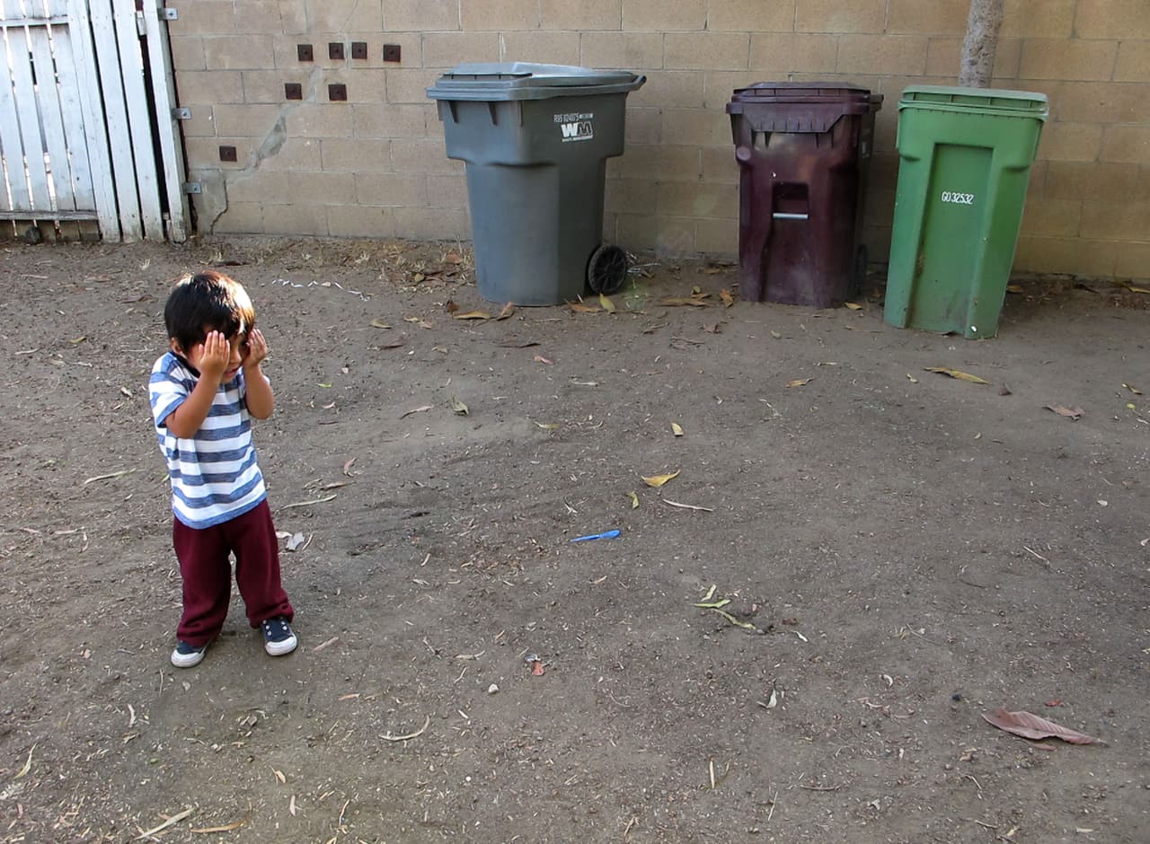 En una escena poco común, Rubén, el hijo de dos años de Nalleli Garrido, juega al escondite en el patio delantero de su casa en Logan Barrio, en Santa Ana, en 2018. La familia luego se mudó para evitar la contaminación debido al plomo en el terreno.