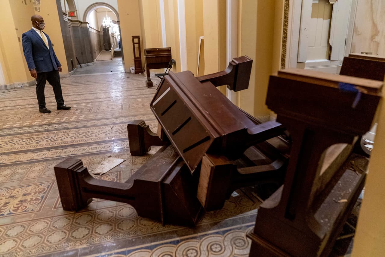 Al día siguiente de este histórico incidente, empleados del Congreso comenzaron a recoger los escombros que dejaron los partidarios de Trump en el Capitolio. En la fotografía el senador republicano Tim Scott en uno de los pasillos donde quedaron algunos muebles apiñados.
<br>