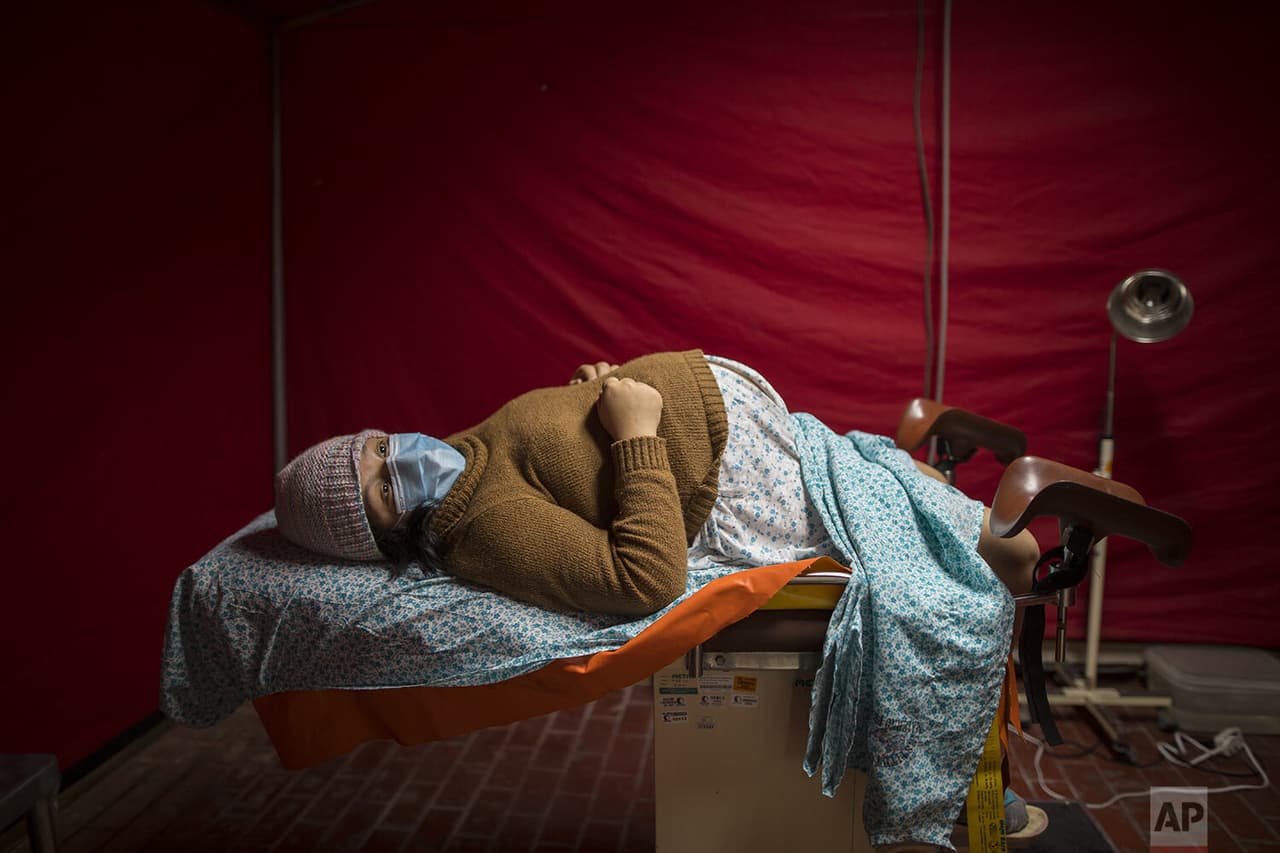 Olinda Tafur, de 20 años, acostada en una mesa de exploración mientras espera ser atendida
<b> dentro de una carpa roja instalada en el área de emergencia del centro</b> para recibir a mujeres en trabajo de parto infectadas.
<br>