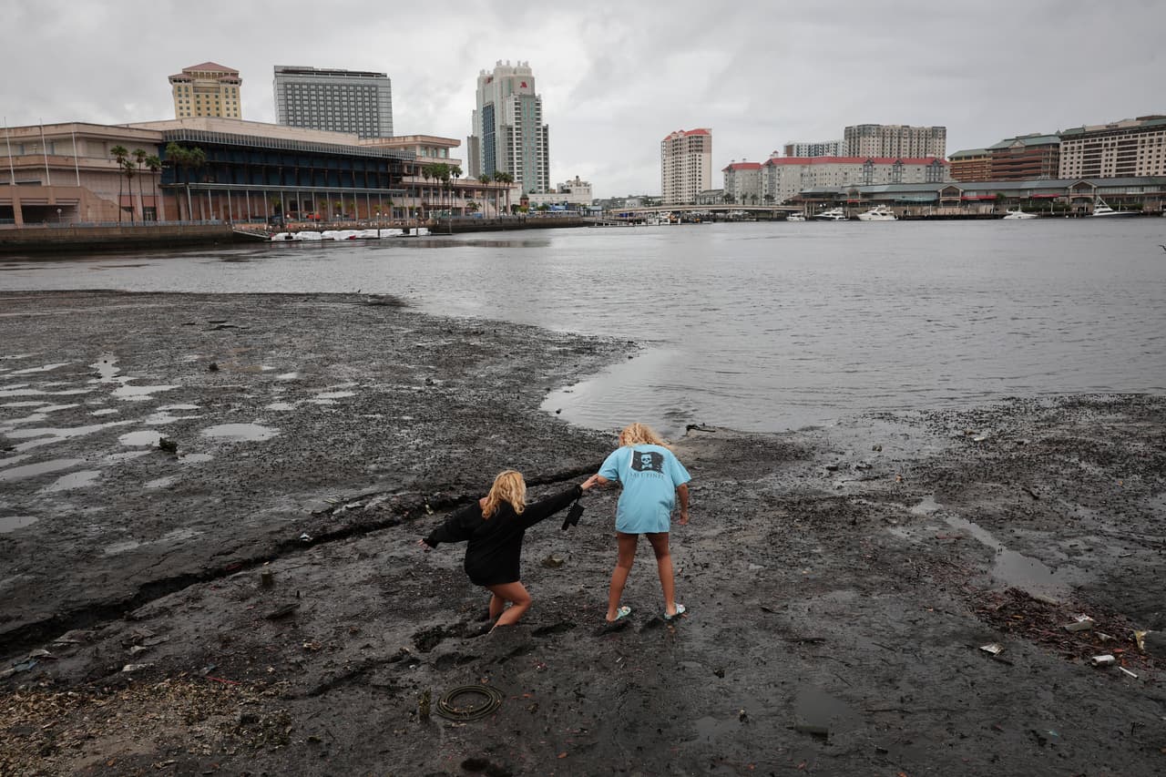 Dos personas caminan sobre la costa en Tampa Bay, donde el mar retrocedió horas antes del embate de Ian. 
<a href="https://www.univision.com/noticias/huracanes/por-que-agua-se-aleja-costa-previo-llegada-huracan-ian" target="_blank">Aquí te explicamos por qué ocurre este fenómeno.</a>