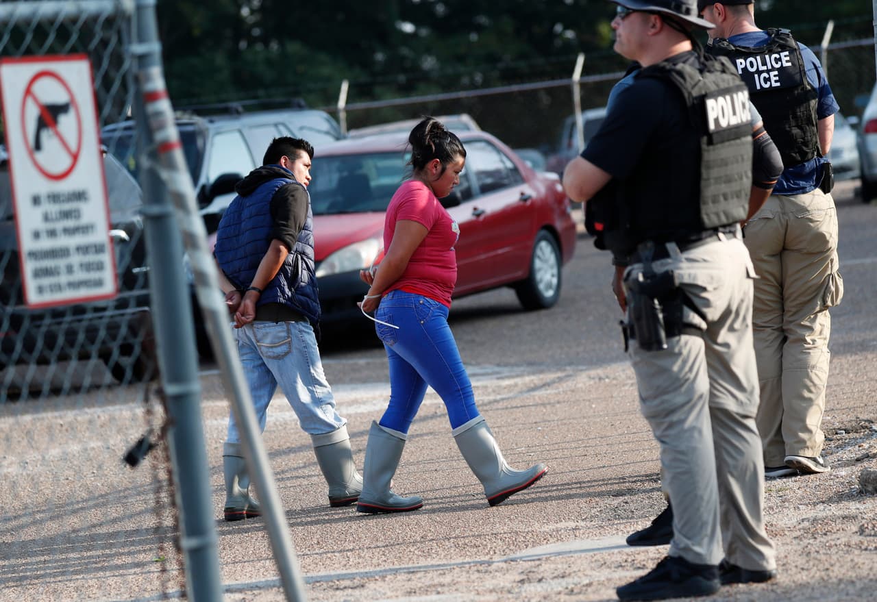 Dos personas son custodiadas por las autoridades migratorias luego de ser arrestados durante la redada.