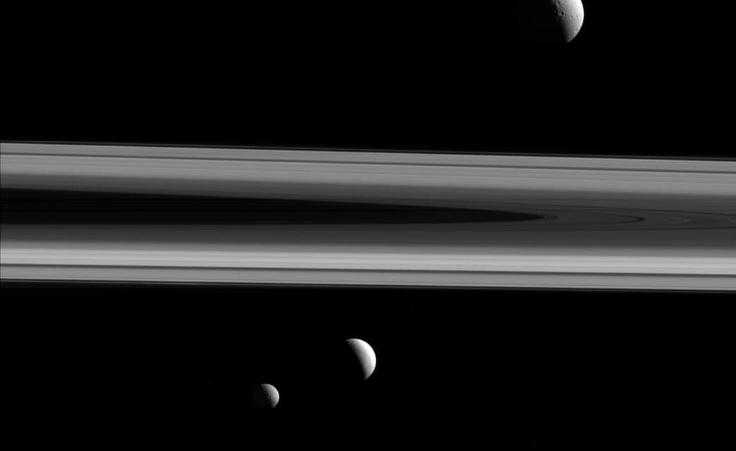 Esta fotografía muestra a tres de las lunas de Saturno: Tetis (por encima de los anillos), Enceladus (al centro) y Mimas (debajo). Fue tomada a 837,000 millas de Enceladus, la más cercana a la Sonda Cassini, parte de un proyecto de cooperación espacial entre la NASA, la Agencia Espacial Europea y la Agencia Espacial Italiana.
