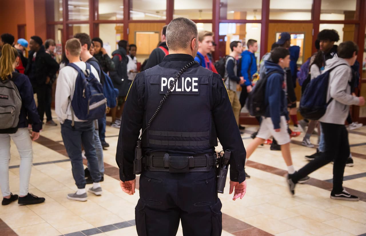 Un oficial de seguridad escolar en South Portland, Maine, se ubica en frente de la oficina principal, mientras los estudiantes se van por el fin de semana, en 2018.