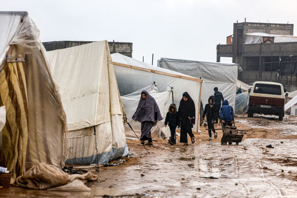 Palestinos desplazados caminan entre las tiendas mojadas de un campamento en Rafah.