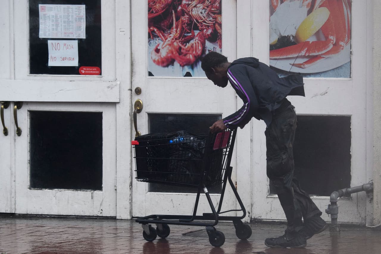 Una persona empuja un carrito de compras a través de la lluvia y los fuertes vientos frente a un restaurante cerrado en Canal Street en Nueva Orleans, Louisiana.