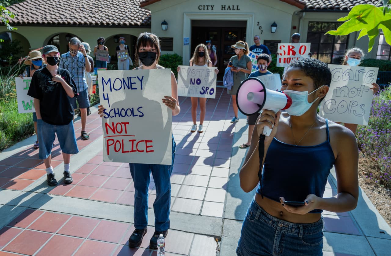 La integrante de la Coalición para la Equidad Estudiantil en Claremont, Jayla Sheffield, entona con megáfono en mano consignas durante la protesta de más de 30 personas en la que se pidió detener el financiamiento de los oficiales de recursos escolares en el Distrito Escolar Unificado de Claremont, el 12 de julio de 2021.