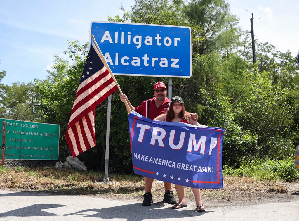 David Mourer y Rana Mourer posan para una foto frente a un cartel que dice Alcatraz de los Caimanes a las afueras del Centro de Entrenamiento y Transición Dade-Collier. Funcionarios estatales de Florida y seguidores de las políticas migratorias del expresidente Donald Trump defienden el centro como una 
<b>medida efectiva para disuadir la inmigración irregular</b>, asegurando que cumple con todos los estándares legales de detención.
