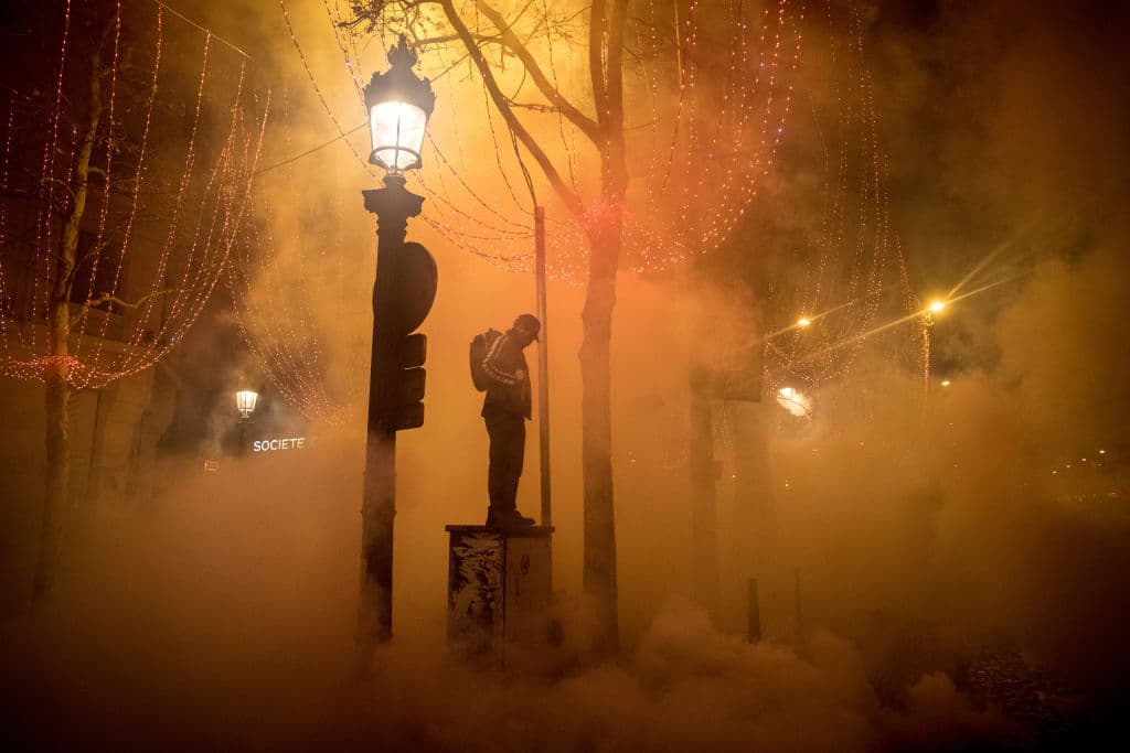 Un manifestante se mantiene en pie elevado sobre un pedestal entre nubes de gas lacrimógeno.