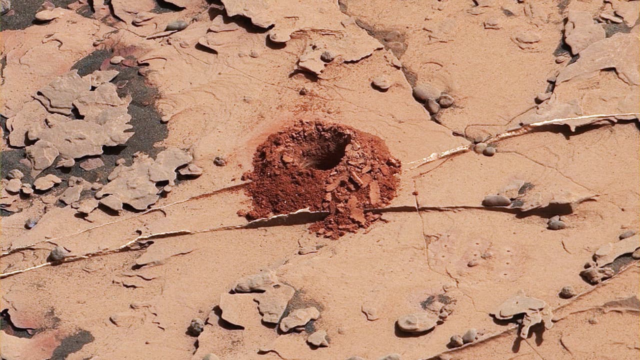 Este agujero en el suelo marciano lo realizó el rover Curiosity a mediados de 2018. Los ingenieros de NASA diseñaron una nueva técnica de perforación luego que el instrumento tuviera un problema mecánico. El hoyo tiene aproximadamente 0,6 pulgadas (1,6 centímetros) de diámetro y fue la primera muestra de roca capturada por el taladro del rover desde octubre de 2016, cuando se descompuso.