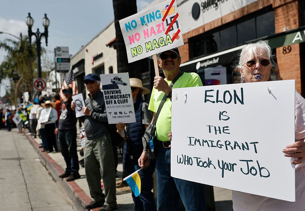 <b>"Elon (Musk) es el inmigrante que te quitó el trabajo"</b>, lee en español esta pancarta en primer plano, aludiendo al origen del empresario multimillonario y mano derecha del presidente Donald Trump.