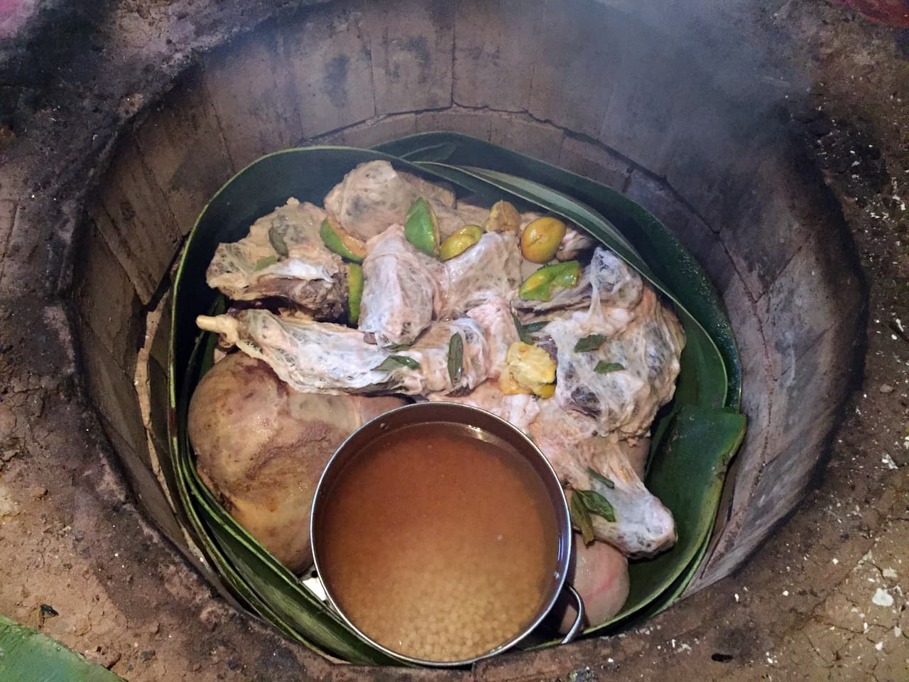 Así se ve la barbacoa acomodada y lista para cocerse en el horno. Al fondo están las panzas rellenas de vísceras, encima los trozos de carne de borrego, envuelta en membranas de grasa, bañada en jugos de naranja y acompañada de hojas de aguacate. En el mismo horno se ponen a cocer los garbanzos que acompañan el consomé de barbacoa.