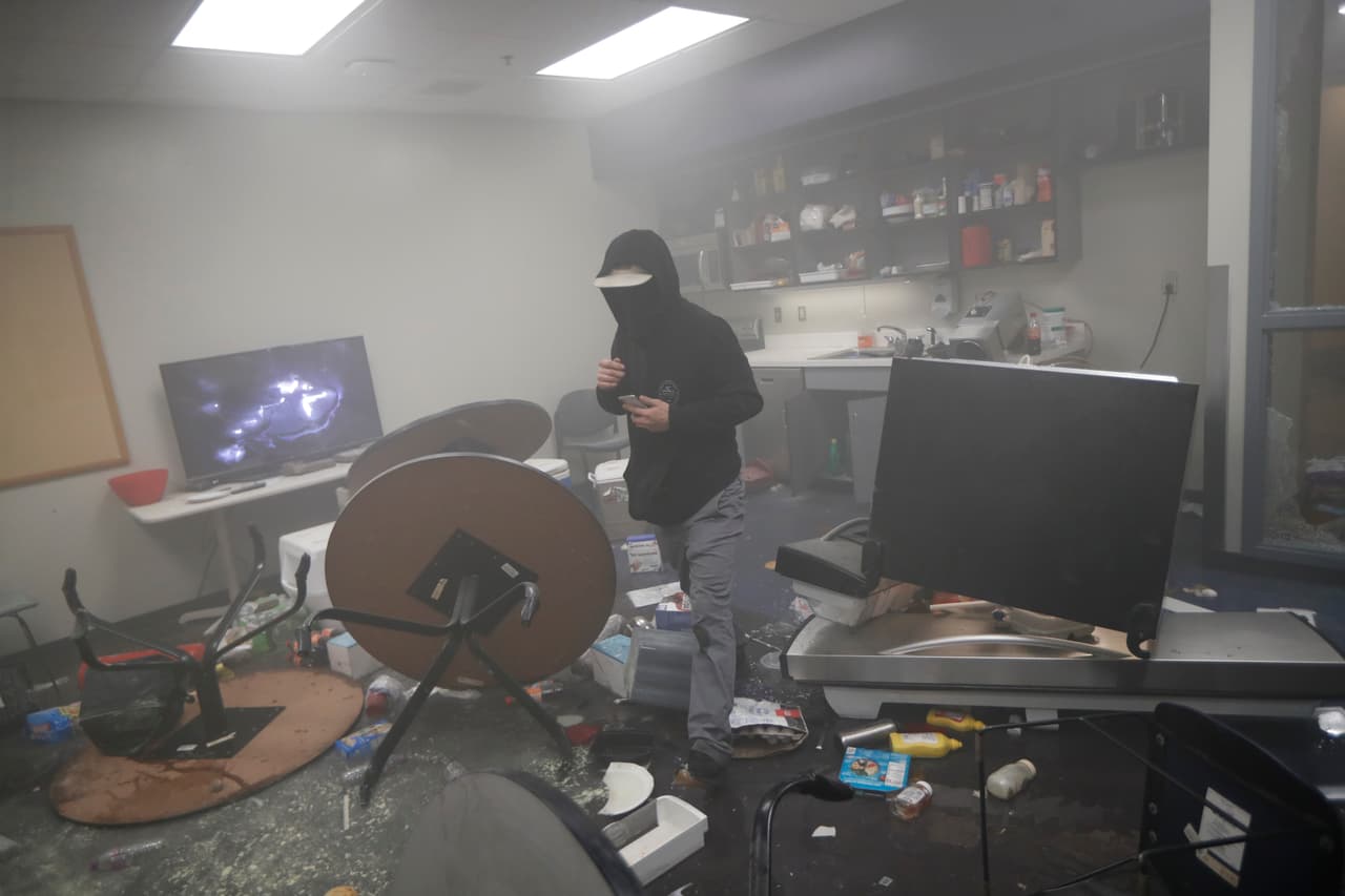 Uno de los manifestantes se mueve dentro de una oficina del tercer precinto policial de Minneapolis en que que se visualizan los destrozos del mobiliario.