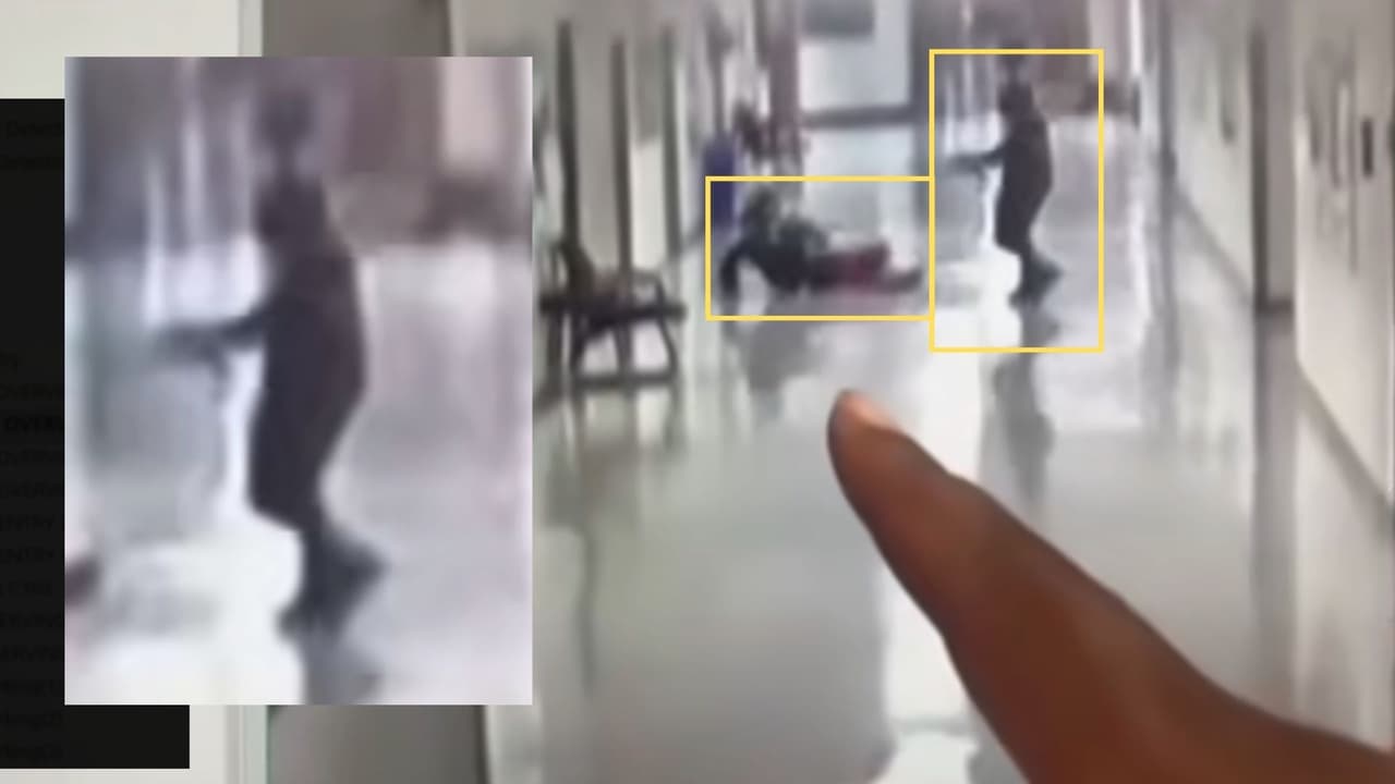 Nuevamente, la persona señala algo en la pantalla: esta vez, es 
<b>el joven con la capucha acercándose con lo que parece ser un arma de fuego</b> al estudiante que permanece en el suelo.