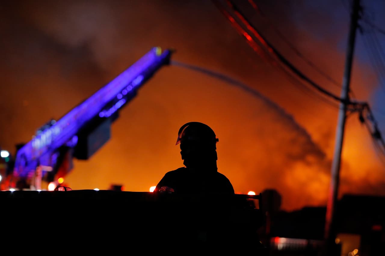 Una policía permanece alerta mientras los bomberos trabajan sofocando los incendios causados por fúricos manifestantes en el tercer día de protestas en Minneapolis.