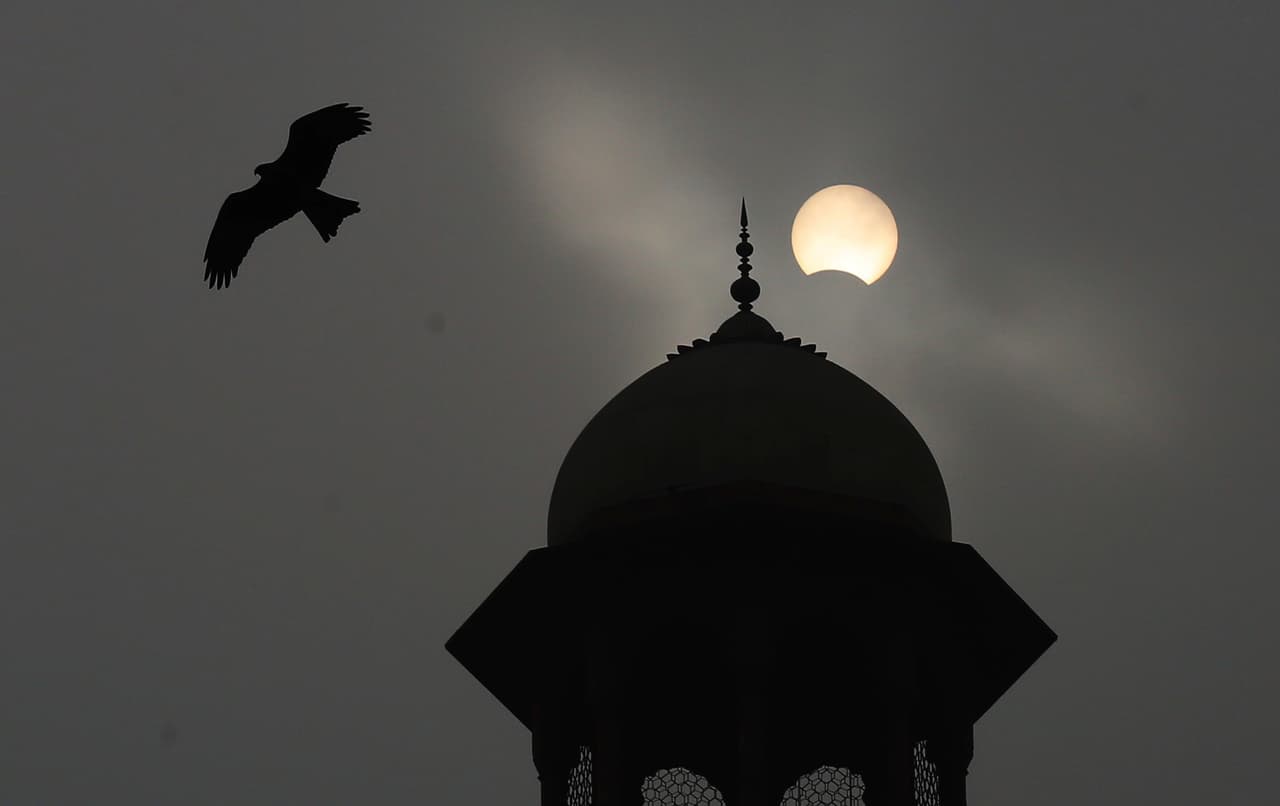 Una ave surca el cielo de Islamabad, Pakistán, cuando apenas la Luna ha empezado a cubrir al Sol.