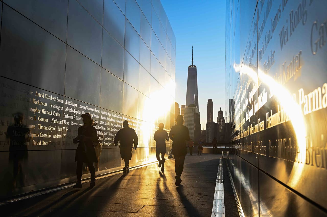 Visitantes caminan al amanecer en el Empty Sky 9/11 Memorial en Jersey City, en el que están inscritos los nombres quienes murieron el 
<a href="https://www.univision.com/noticias/20-anos-atentados-9-11/atentados-del-11-de-septiembre-de-2001-9-11-torres-gemelas-20-anos-despues">11 de septiembre</a> de 2001 en el ataque en la vecina ciudad de Nueva York. Al fondo se ve la WTC1, la torre que se edificó donde estuvieron las torres gemelas.