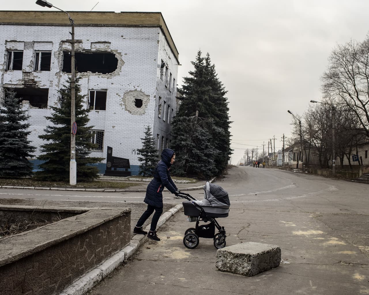 Una mujer camina con su bebé en un coche por la calle Lenin. Atrás se ve una estación de policía que quedó destruida en un combate en 2014 en Donbas, Ucrania.