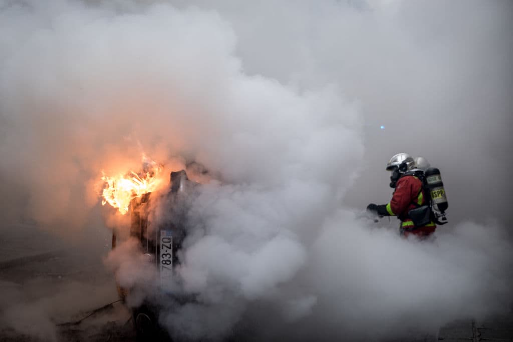Un bombero trata de extinguir un auto en llamas en medio de la manifestación.