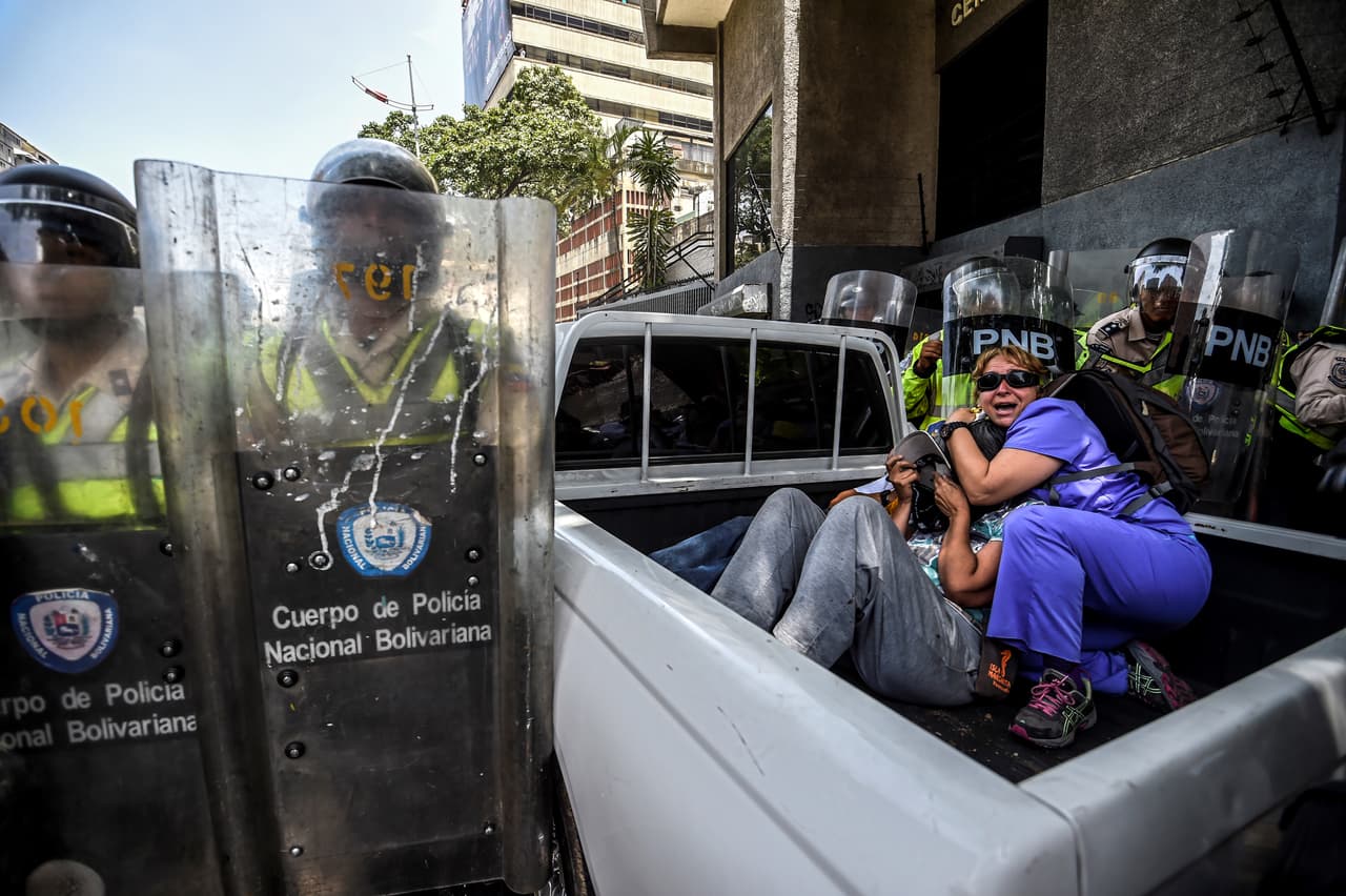 Algunos intentan protegerse de los objetos contundentes lanzados por los manifestantes y la respuesta con gas y perdigones de la policía.