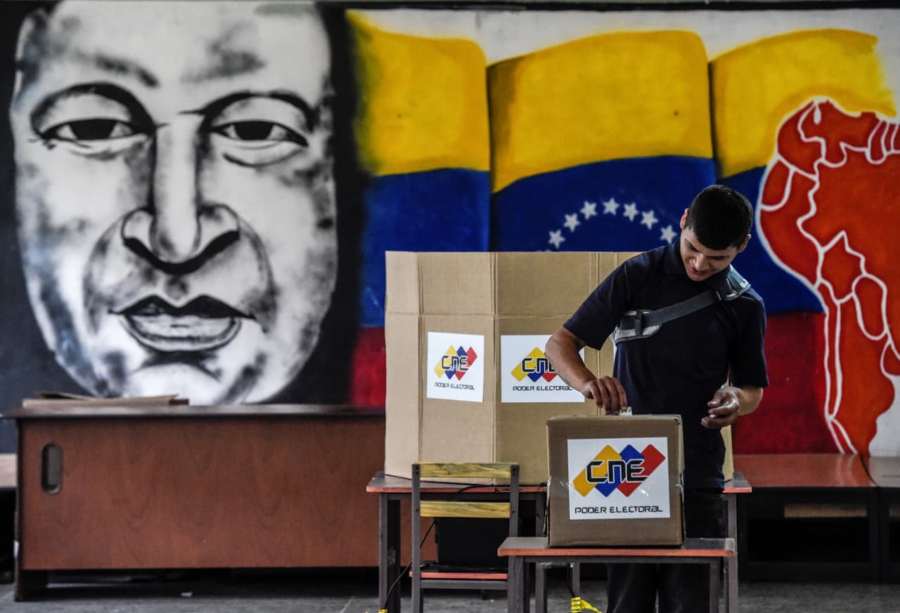 Un elector deposita su voto frente a un mural del difunto presidente Hugo Chávez.