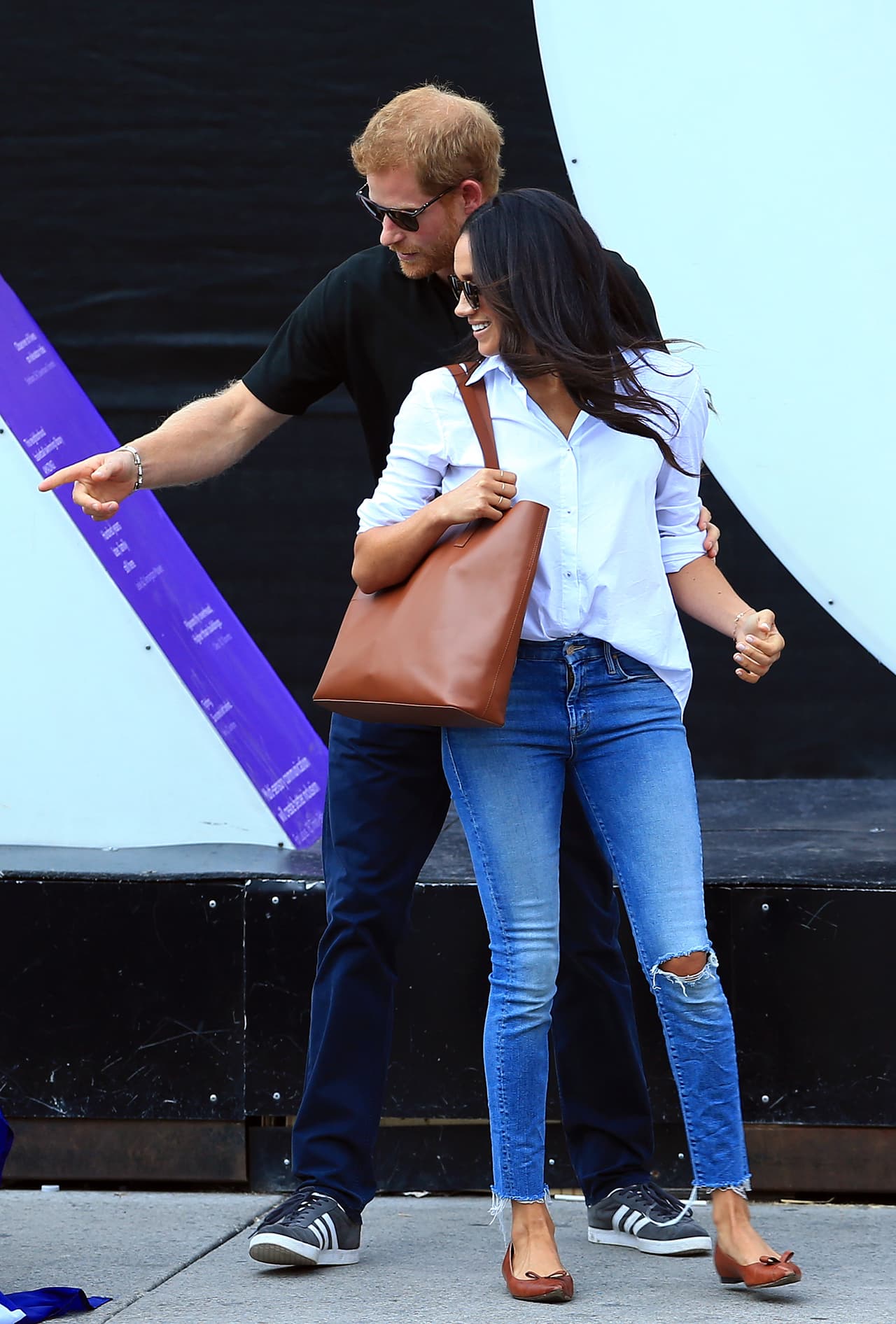 <b>Septiembre, 2017</b>
<br>Al día siguiente, vimos a la pareja por primera vez juntos en los Invictus Games en Toronto, Meghan eligió la camisa blanca "Husband' de la diseñadora 
<b>Misha Nonoo</b> y unos jeans rotos en la rodilla que acompañó con accesorios Everlane.
