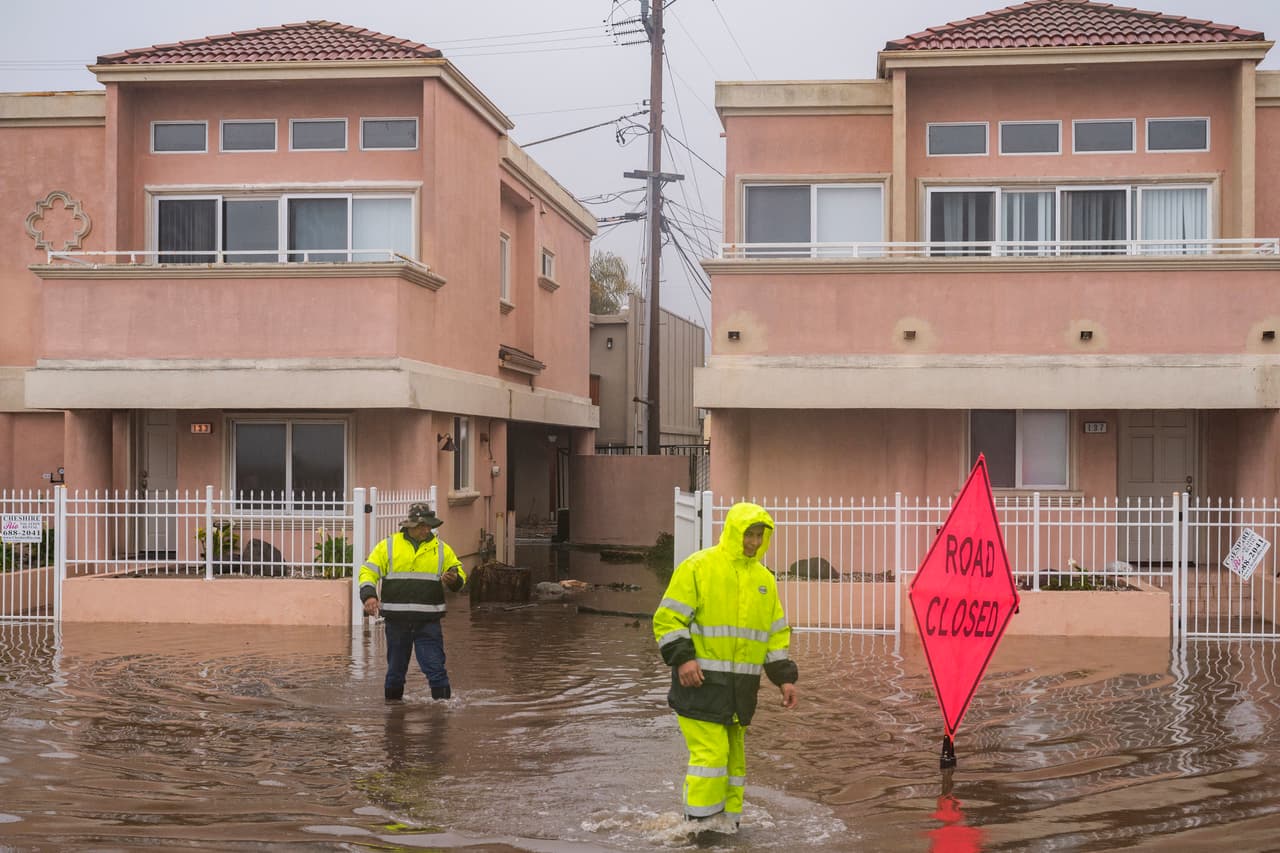 El paso de 
<a href="https://www.univision.com/noticias/estados-unidos/california-espera-tormentas-severas-causadas-rios-atmosfericos" target="_blank">las tormentas en California</a> ha dejado al menos 14 muertos y ha obligado la evacuación de comunidades enteras. Al menos 95,000 personas continuaban sin energía eléctrica en la noche de este lunes, según el sitio poweroutage.us. En la imagen, equipos de limpieza caminan en el barrio Rio Del Mar en Aptos, California.