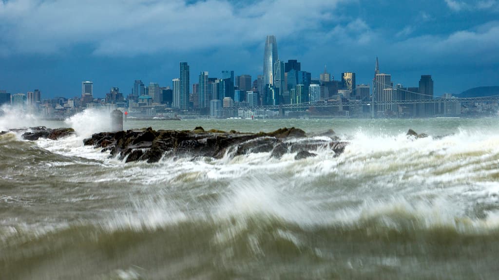 Las olas rompen sobre un rompeolas en Alameda, California, con el horizonte de San Francisco al fondo el domingo 4 de febrero de 2024. Los fuertes vientos y las fuertes lluvias están afectando la región. (Foto AP/Noah Berger)