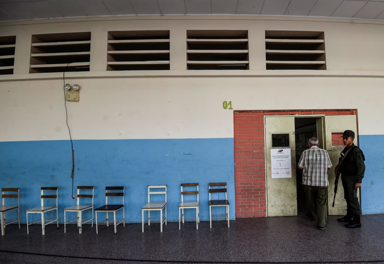 Un hombre se dirige a su mesa de votación, bajo la mirada de un soldado.