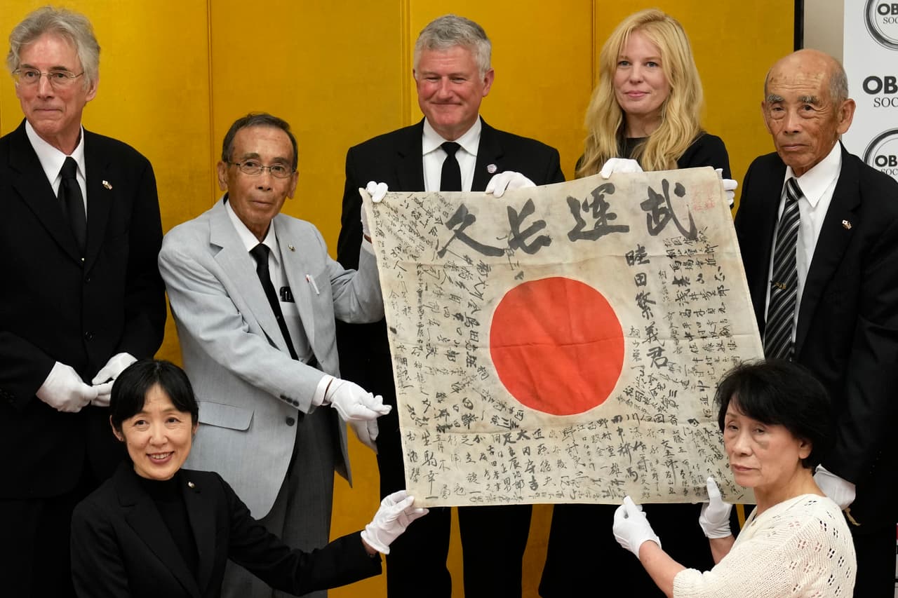 El director ejecutivo del USS Lexington Museum, Steve Banta, centro, tres hijos del soldado japonés Shigeyoshi Mutsuda, Toshiyuki Mutsuda, derecha, Misako Matsukuchi, abajo a la derecha, Yasunori Matsuda, tercero a la izquierda, posan con la bandera de la buena suerte de Mutsuda durante la ceremonia de entrega en el santuario Yasukuni en Tokio, Japón, sábado 29 de julio de 2023.