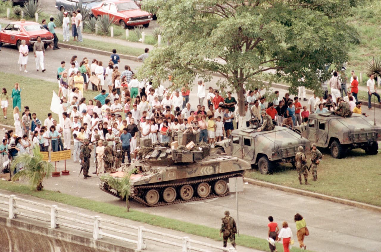 U tanque y dos vehículos blindados del ejército de los EEUU forman un bloqueo en la avenida Balboa de la ciudad de Panamá, que conduce hacia la embajada del Vaticano el miércoles 27 de diciembre de 1989, donde Manuel Noriega ha buscado refugio. Una multitud de manifestantes anti-Noriega se reúnen alrededor de los tanques.