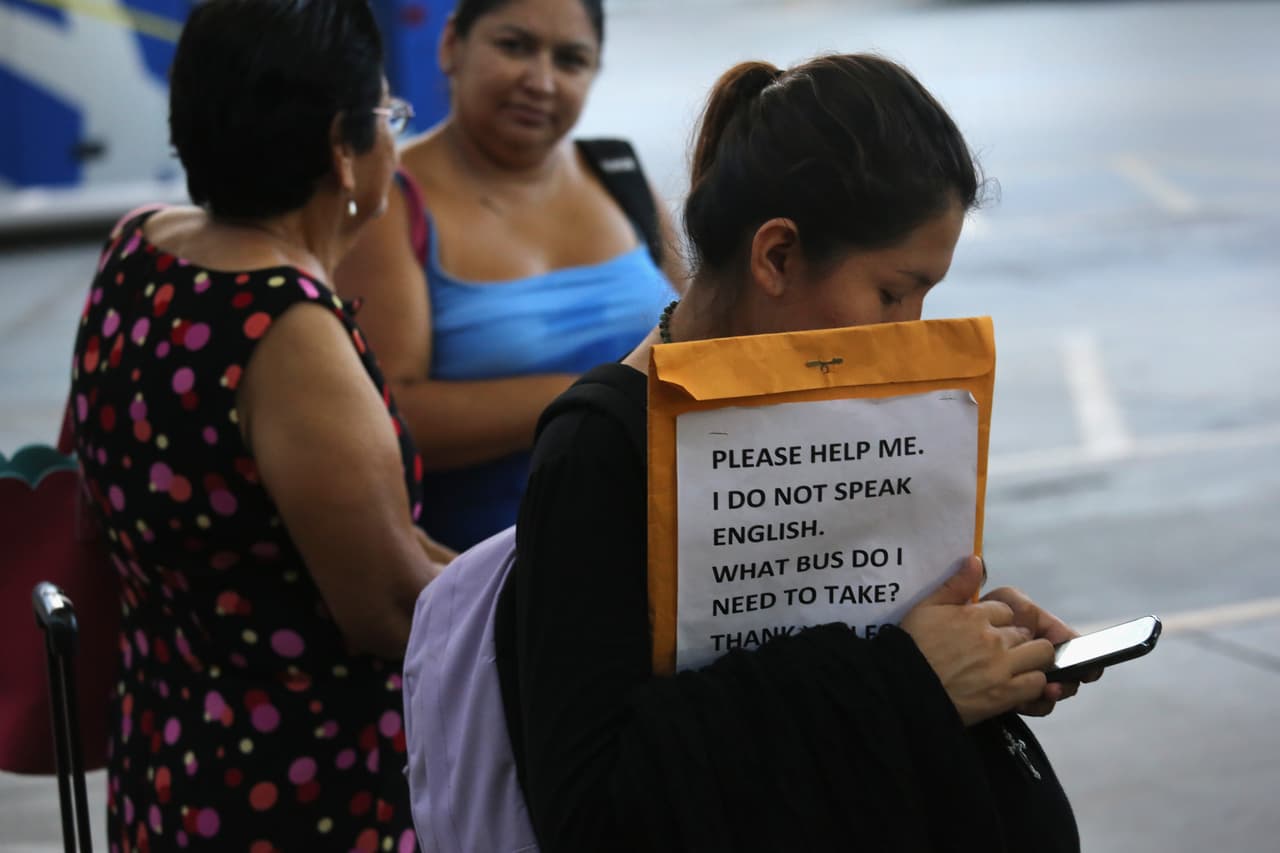 Una inmigrante indocumentada embarazada, de origen centroamericano, como parte de la preparación de su viaje dentro de los Estados Unidos, lleva un cartel escrito en Inglés en el que se lee: “Por favor ayúdeme, yo no hablo inglés, ¿qué autobús debo tomar?".
<br>