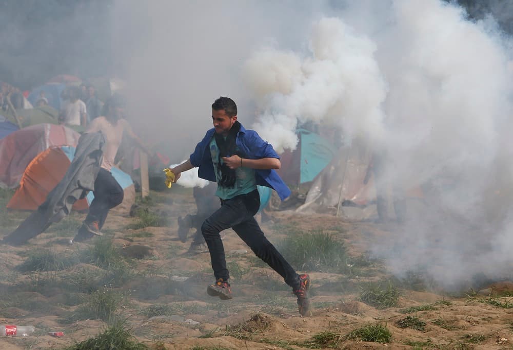 Un joven corre con un cartucho de gas lacrimógeno lanzado por las autoridades tras su intento de seguir hacia otros países europeos.