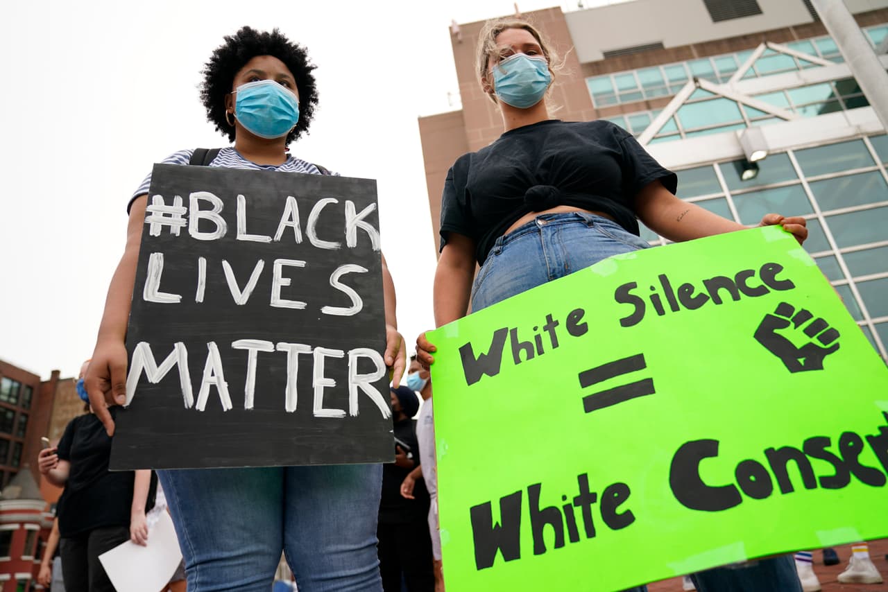 Un par de 
<a href="https://www.univision.com/temas/manifestaciones">manifestantes</a> se reúne para protestar por la muerte de George Floyd en la esquina de las calles 14 y U en Washington, este 29 de mayo de 2020. Llevan carteles del movimiento #BlackLivesMatter, mientras la joven blanca lleva una pancarta en la que se lee que el silencio blanco es igual al consentimiento.