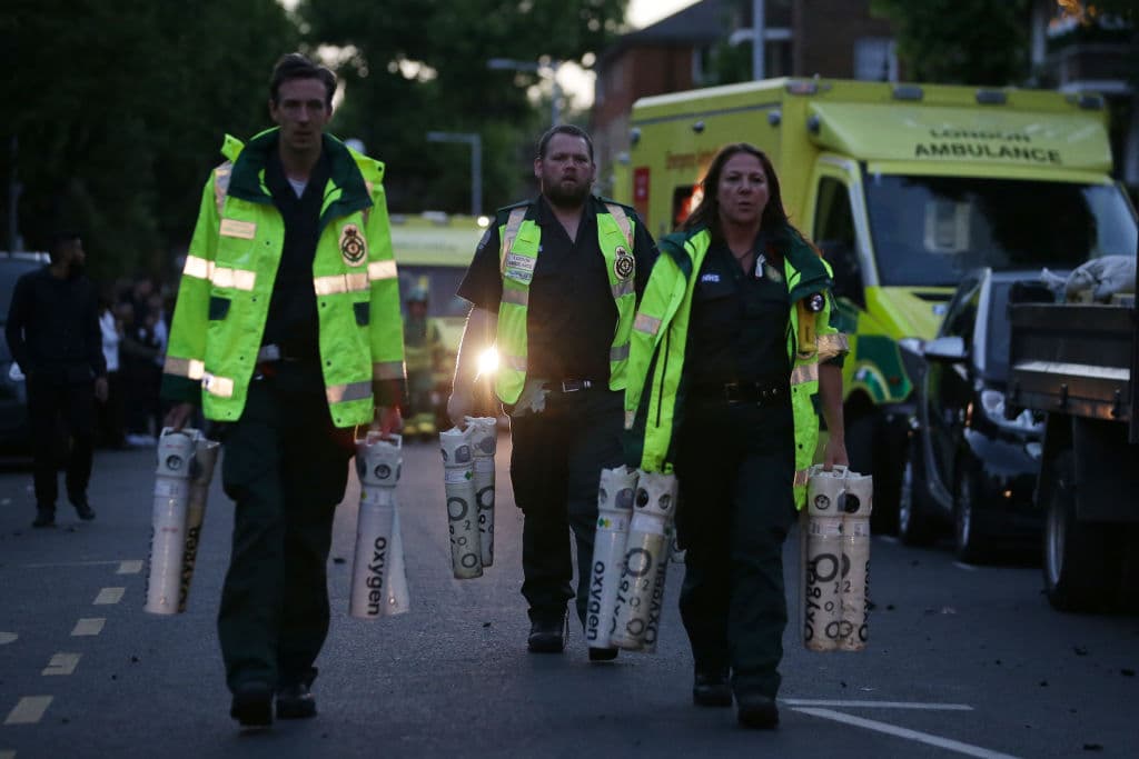 Personal paramédicos lleva bombonas de oxígenos para asistir a los posibles vecinos asfixiados con el humo del incendio en el edificio de Londres