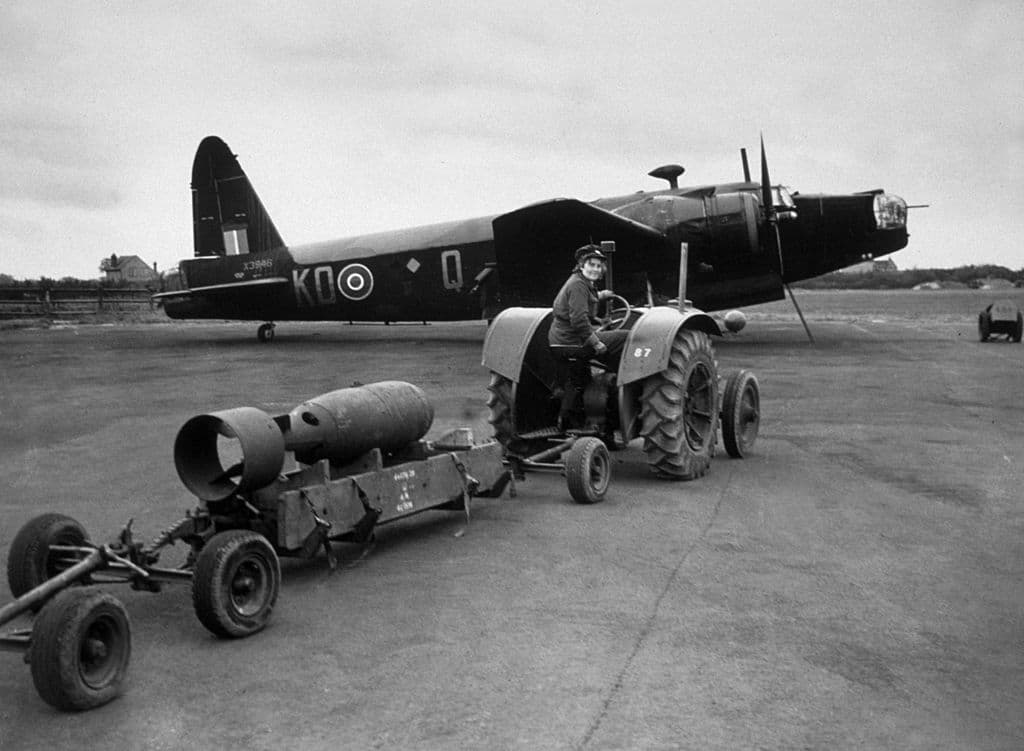 A member of the Women's Auxiliary Air Force (WAAF) hauling a bomb to an awaiting Vickers Wellington MkIII bomber in April 1942.