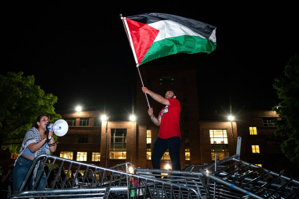 Un joven sostiene una bandera palestina mientras activistas y estudiantes cantan, en un campamento en la Universidad George Washington el 29 de abril de 2024 en Washington DC. Las protestas universitarias se extendieron por todo Estados Unidos y luego por el mundo, en 
<a href="https://www.univision.com/noticias/mundo/presiones-benajamin-netanayahu-seguir-con-la-guerra-en-gaza-mantenerse-en-el-poder-supervivencia-politica">solidaridad con los palestinos. </a>Los jóvenes pedían a sus universidades que 
<a href="https://www.univision.com/noticias/mundo/israel-guerra-en-gaza-transformacion-de-israel-en-un-estado-paria-analisis-luciano-zaccara">corten vínculos financieros con Israel</a> o con empresas que le financien armas para la guerra.