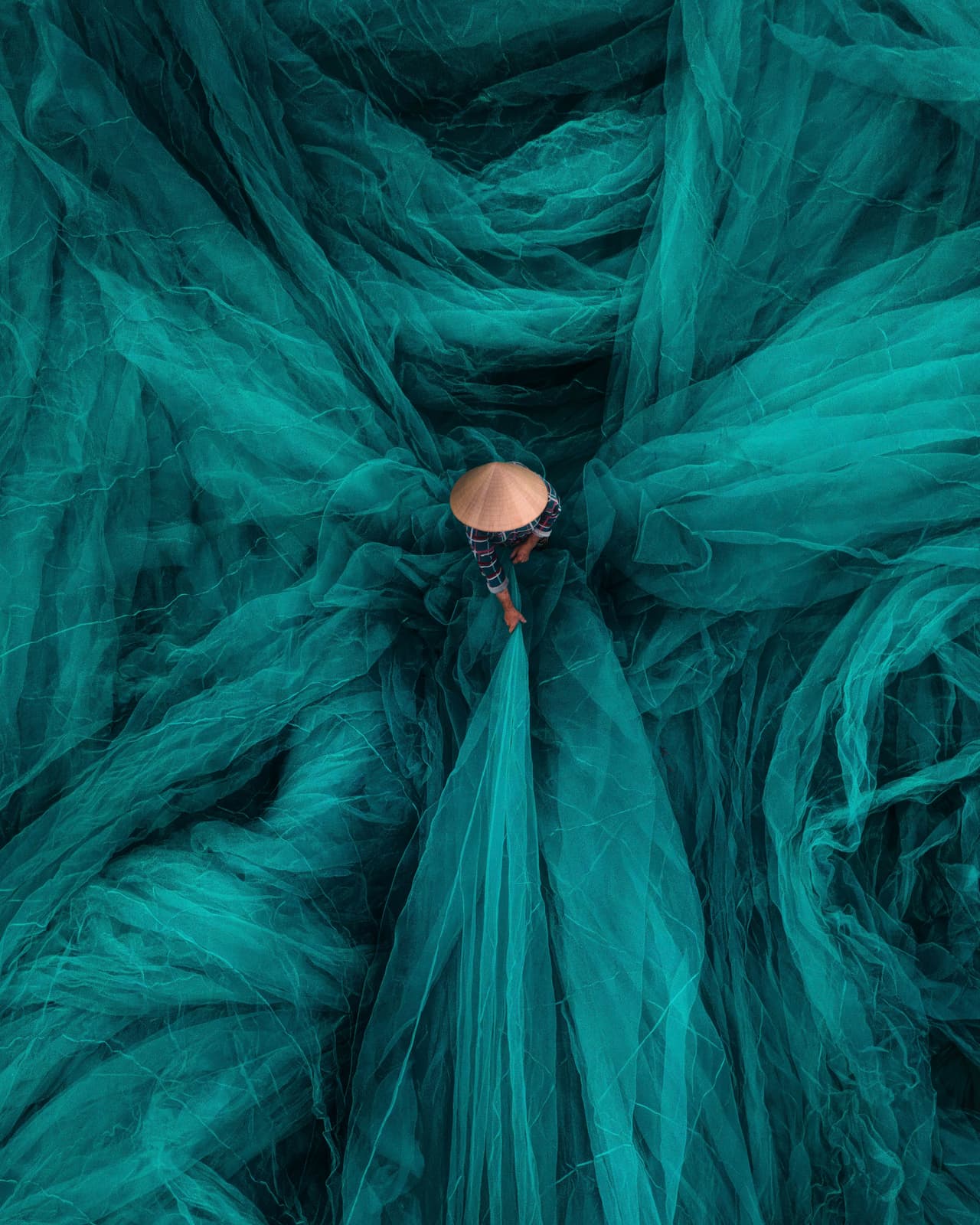 Un artesano vietnamita teje una red de pesca a mano, rodeado de hilos verdes que fluyen; una tradición transmitida de generación en generación.
<br>