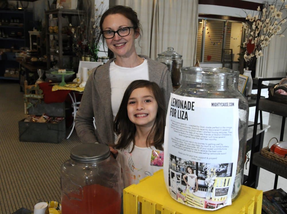 Elizabeth Scott y su hija de 7 años, Liza Scott, que dirige un puesto de limonada para ayudar a financiar su propia cirugía cerebral, se muestran en la panadería de la mujer en Homewood, Alabama.