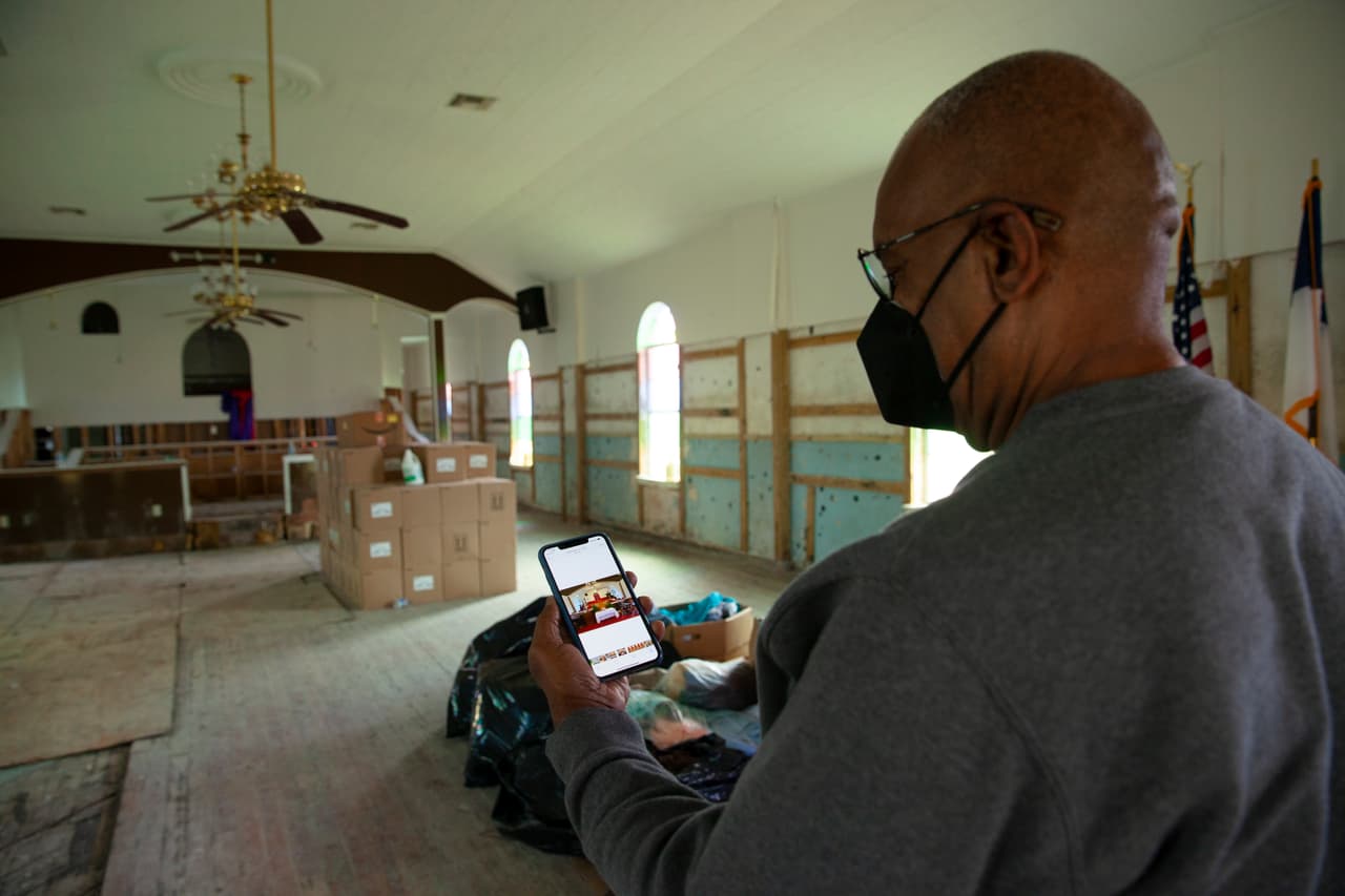 El reverendo Haywood Johnson Jr. compara una fotografía de la Iglesia Bautista Saint Paul Missionary tomada antes del paso del huracán Ida en 2021, con lo que tiene ahora frente a sus ojos. Durante el ciclón, la comunidad de Ironton, Louisiana, se anegó con hasta 16 pies de agua. Johnson y feligreses tuvieron que limpiar la estructura por sí mismos.