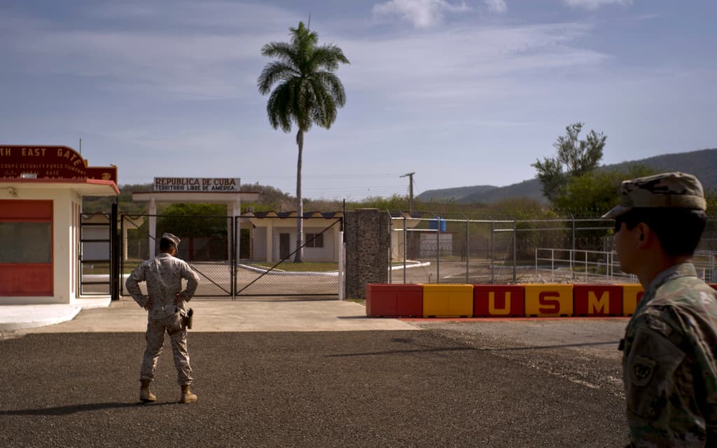 ARCHIVO - En esta fotografía revisada por oficiales militares de Estados Unidos, un soldado del ejército, derecha, y un miembro de la infantería de Marina permanecen frente a las verjas que separan el territorio cubano de la Base Naval estadounidense, el 6 de junio de 2018, en Bahía de Guantánamo, Cuba. (AP Foto/Ramón Espinosa, archivo)