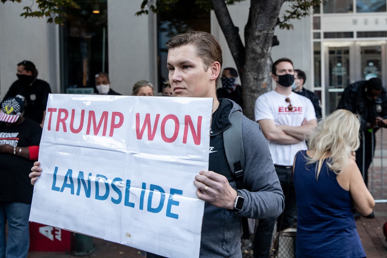 Un partidario del presidente de los EE. UU., Donald Trump, se para con un cartel al otro lado de la calle de personas que celebran fuera del Centro de Convenciones de Filadelfia después de que Joe Biden fuera declarado ganador de las elecciones presidenciales de 2020 el 7 de noviembre de 2020 en Filadelfia, Pensilvania.