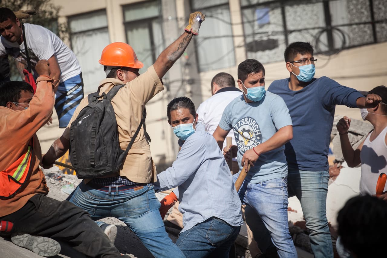 Un grupo de civiles extienden la solicitud de silencio de un experto que explora bajo los escombros en busca de sobrevivientes.
<br>