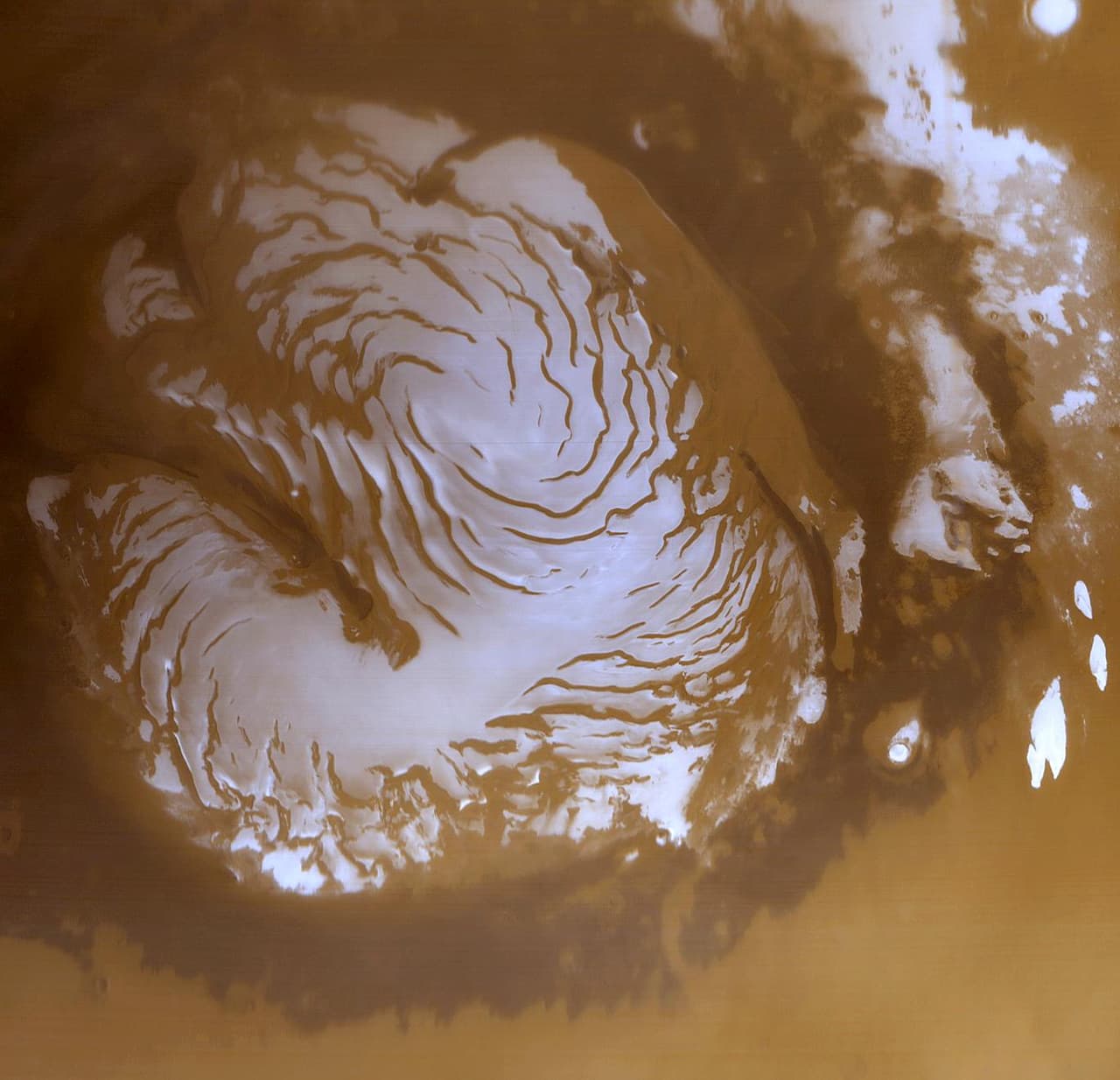 El polo norte marciano durante el verano. Como la Tierra, Marte tiene hielo en sus polos. El agua llega a ellos en forma de vapor, que al mezclarse con el polvo forma capas brillantes y oscuras de hielo ‘limpio’ y ‘sucio’. Durante el invierno las temperaturas son tan bajas que el dióxido de carbono de la atmósfera se congela y forma capas adicionales de ‘hielo seco’.