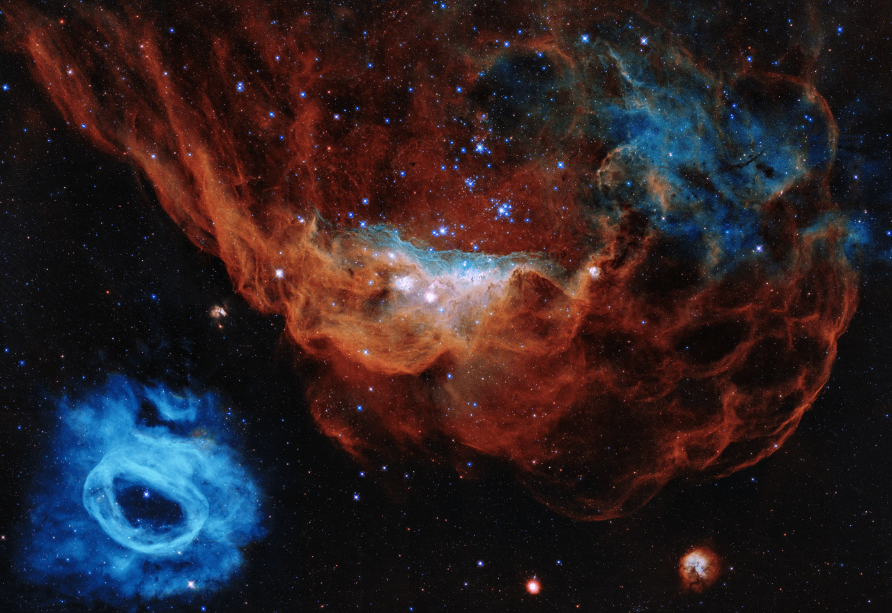 <b>Arrecife Cósmico (año 2020).</b> Esta imagen tomada por el Hubble conmemora los 30 años en el espacio. Allí se ve cómo las estrellas masivas, jóvenes y enérgicas iluminan su lugar de nacimiento con vientos y radiación ultravioleta. La nebulosa roja gigante y su vecino azul más pequeño son parte de una vasta región formadora de estrellas en la Gran Nube de Magallanes, una galaxia satélite de la Vía Láctea, ubicada a 163,000 años luz de distancia.