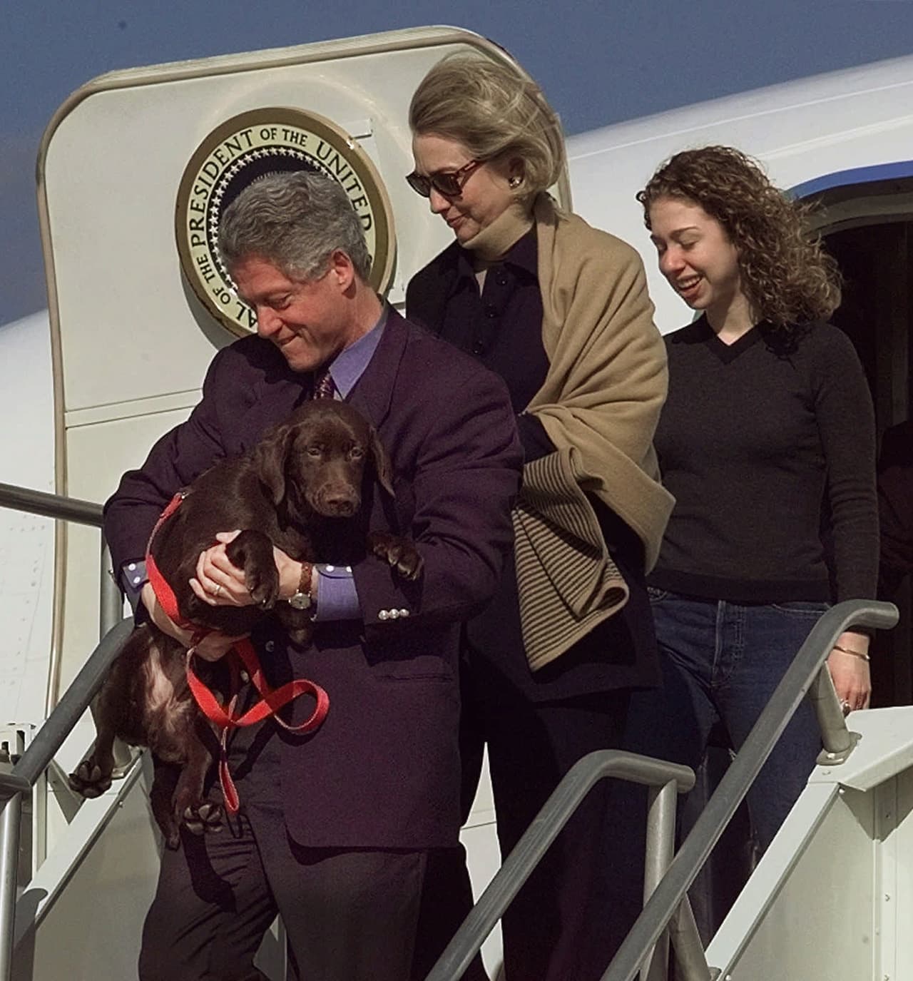 Bill Clinton, su esposa Hillary y su hija Chelsea en la escalinata del Air Force One con su único perro, un 
<i>Labrador Retriever</i> llamado '`Buddy'.