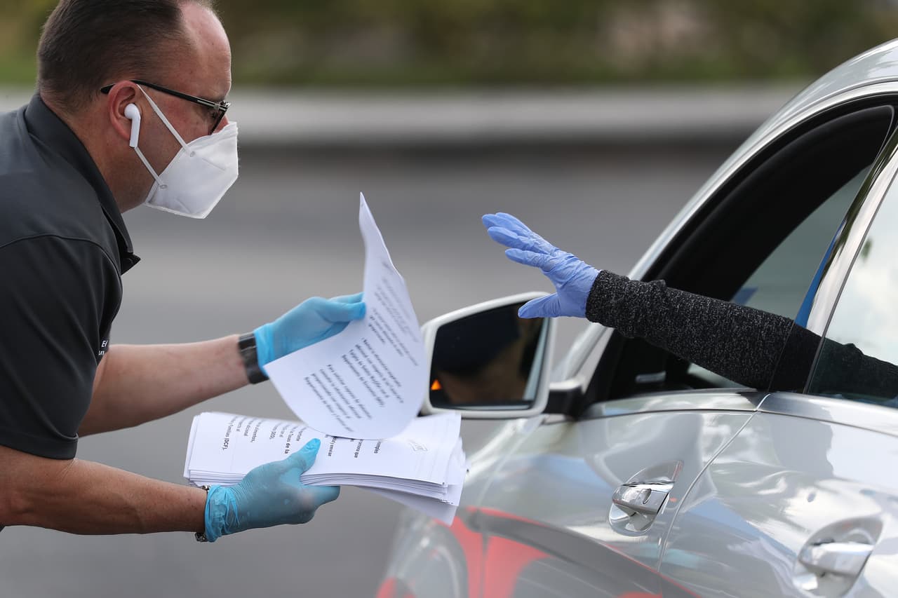 <b>Solicitud de ayuda por desempleo.</b> Una oficial de la ciudad de Hialeah, Florida, entrega planillas a una fila de desempleados en auto, el 8 de abril. Desde que comenzó la crisis unas 
<a href="https://www.univision.com/noticias/dinero/otra-avalancha-3-8-millones-piden-el-subsidio-por-desempleo-en-eeuu-afectados-por-la-pandemia">33.5 millones de personas han solicitado ayuda por desempleo en EEUU</a>.