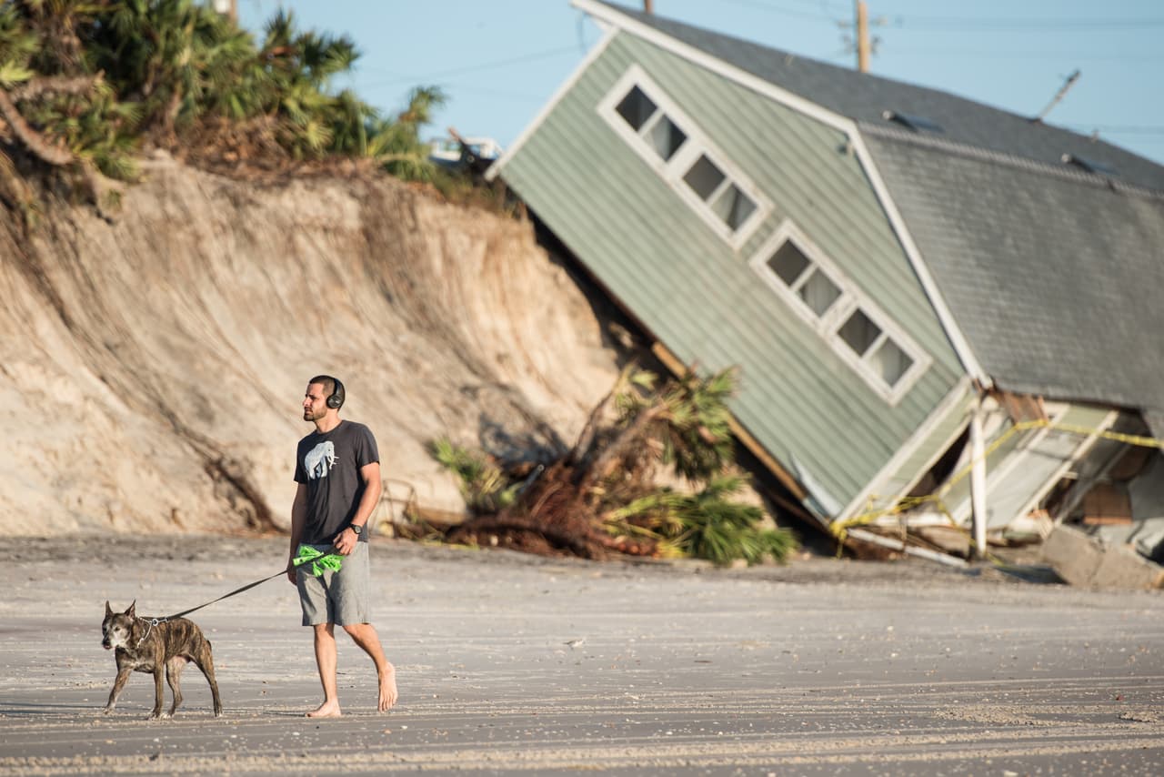 José Orosz pasea a su perra Karen por la playa de Vilano Beach, cerca de Jacksonville. La imagen no tendría nada de llamativo sino fuera que detrás de Orosz una casa completamente destruida y derrumbada sobre el mal son muestra de que el destructivo paso de Irma.