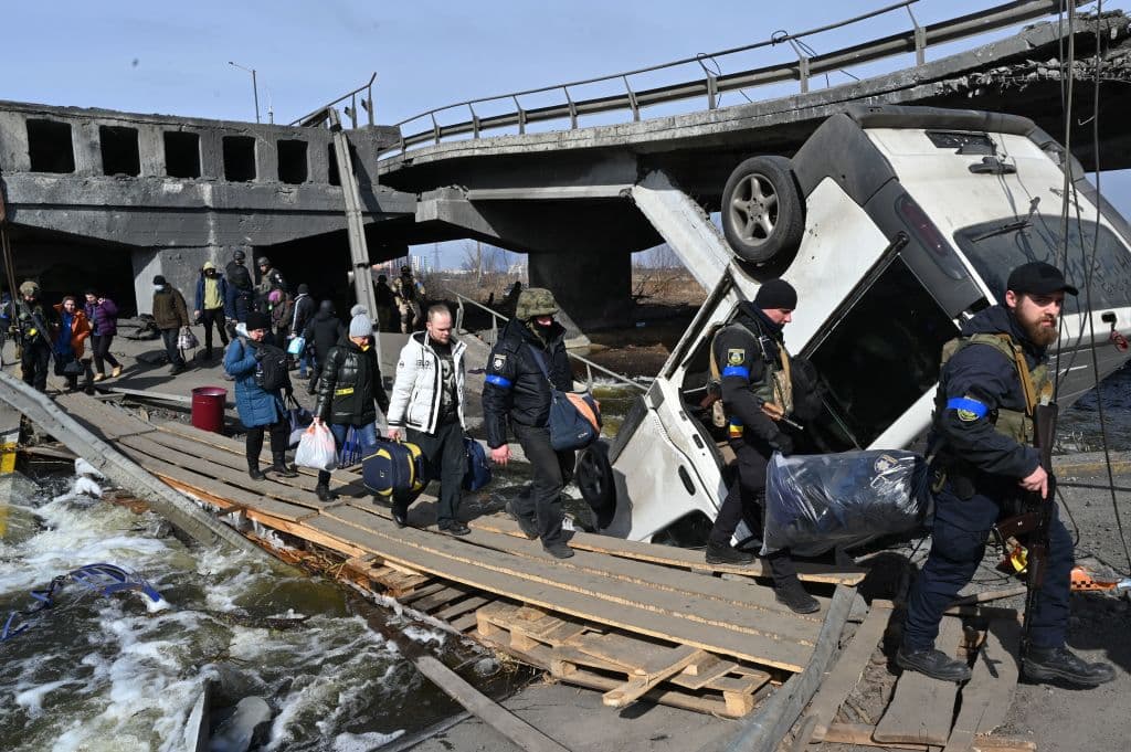 En la imagen, agentes ucranianos ayudan a los residentes a cruzar un puente destruido mientras evacuan Irpin.