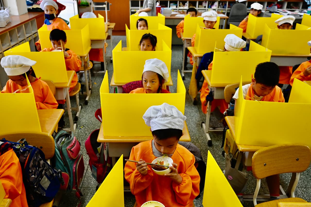 <b>Escritorios con barreras.</b> Los estudiantes de una escuela primaria en Taipei, Taiwan, tomando su almuerzo en el aula el 29 de abril. Allí los escritorios fueron separados con paneles de plástico para mantener la distancia entre los niños. En varios países las escuelas han reabierto, pero existen nuevos procedimientos y precauciones a seguir.